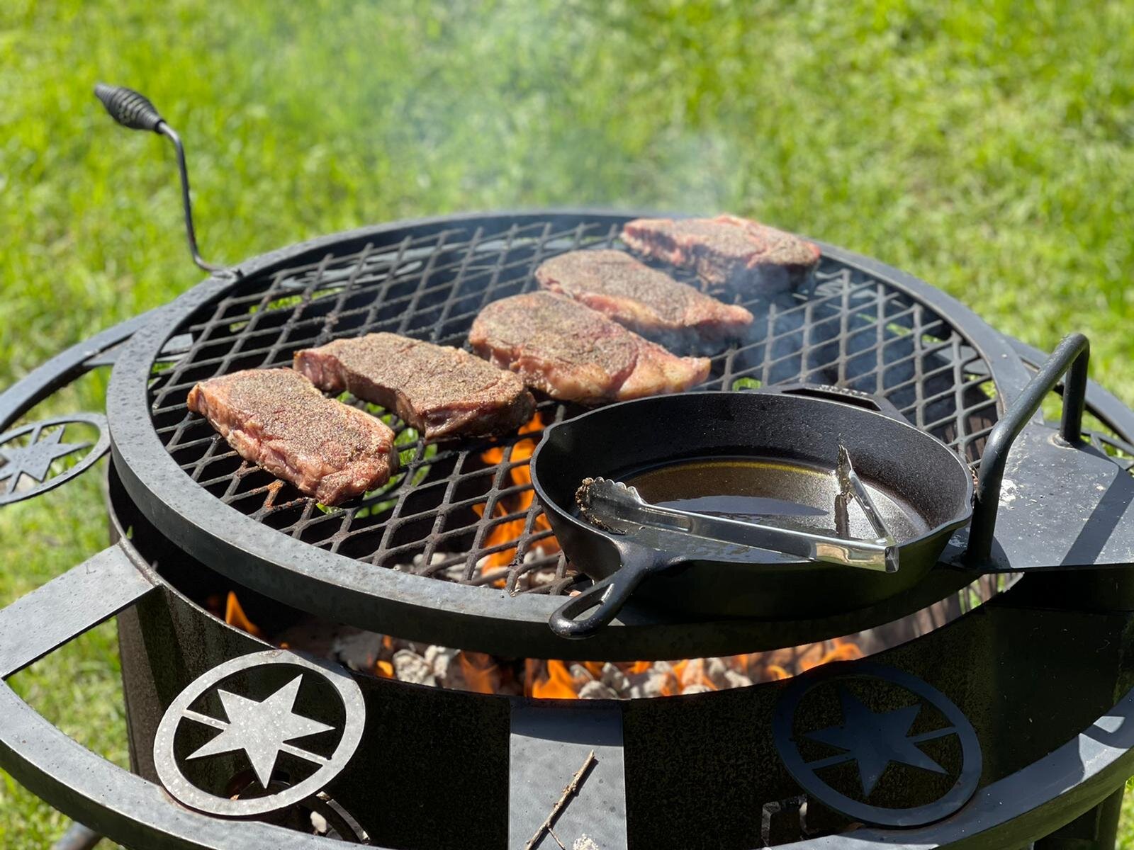 Steaks cooking on firepit with cast iron skillet